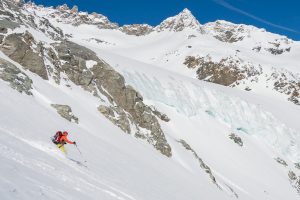 Descente d'un skieur dans la neige fraiche devant un glacier